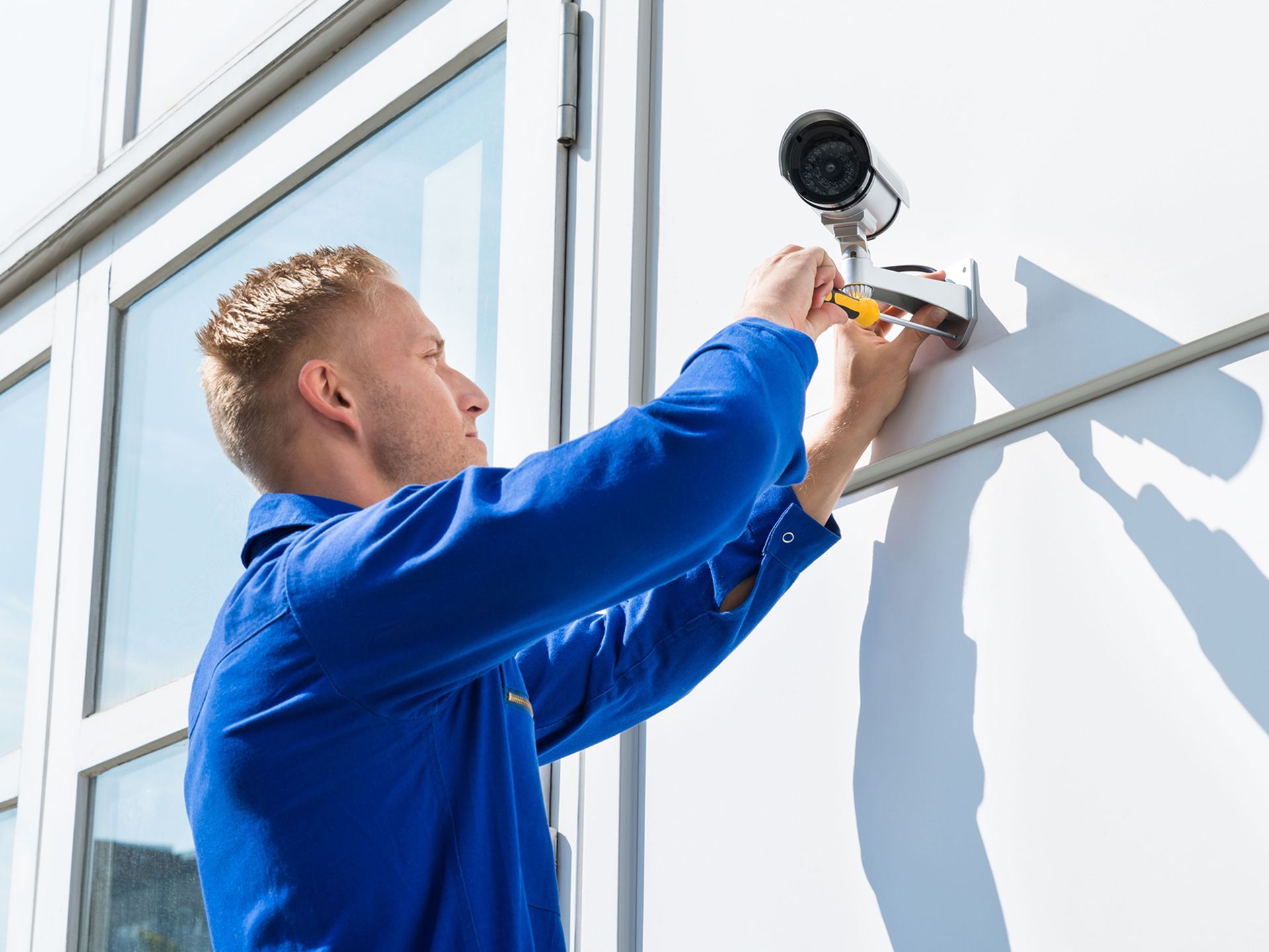 A man is installing a security camera on the side of a building.