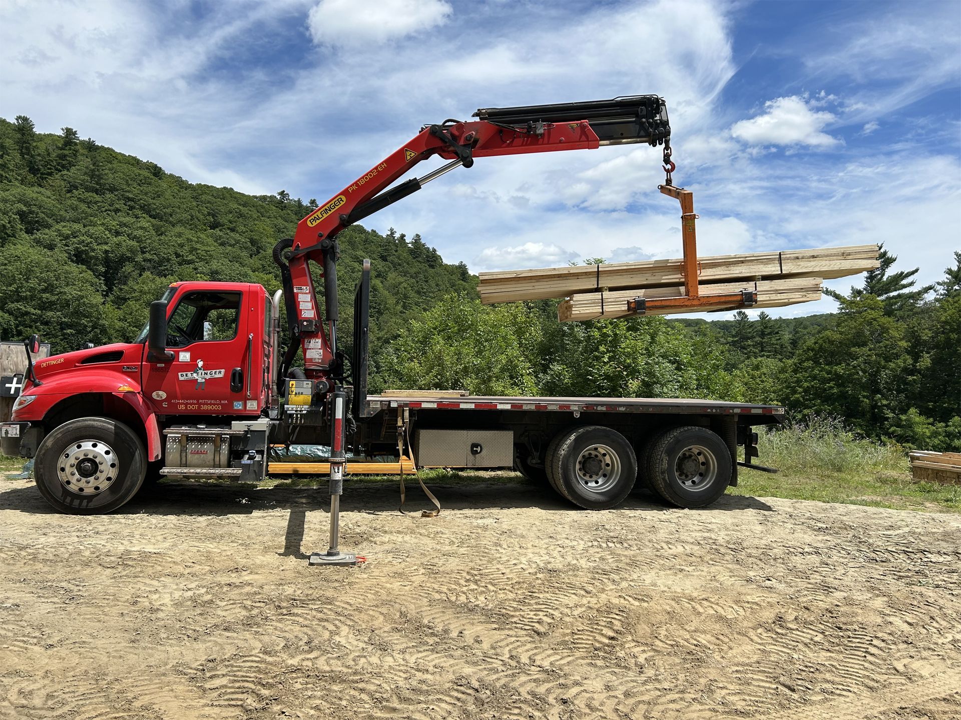 Red truck with crane lifting lumber.