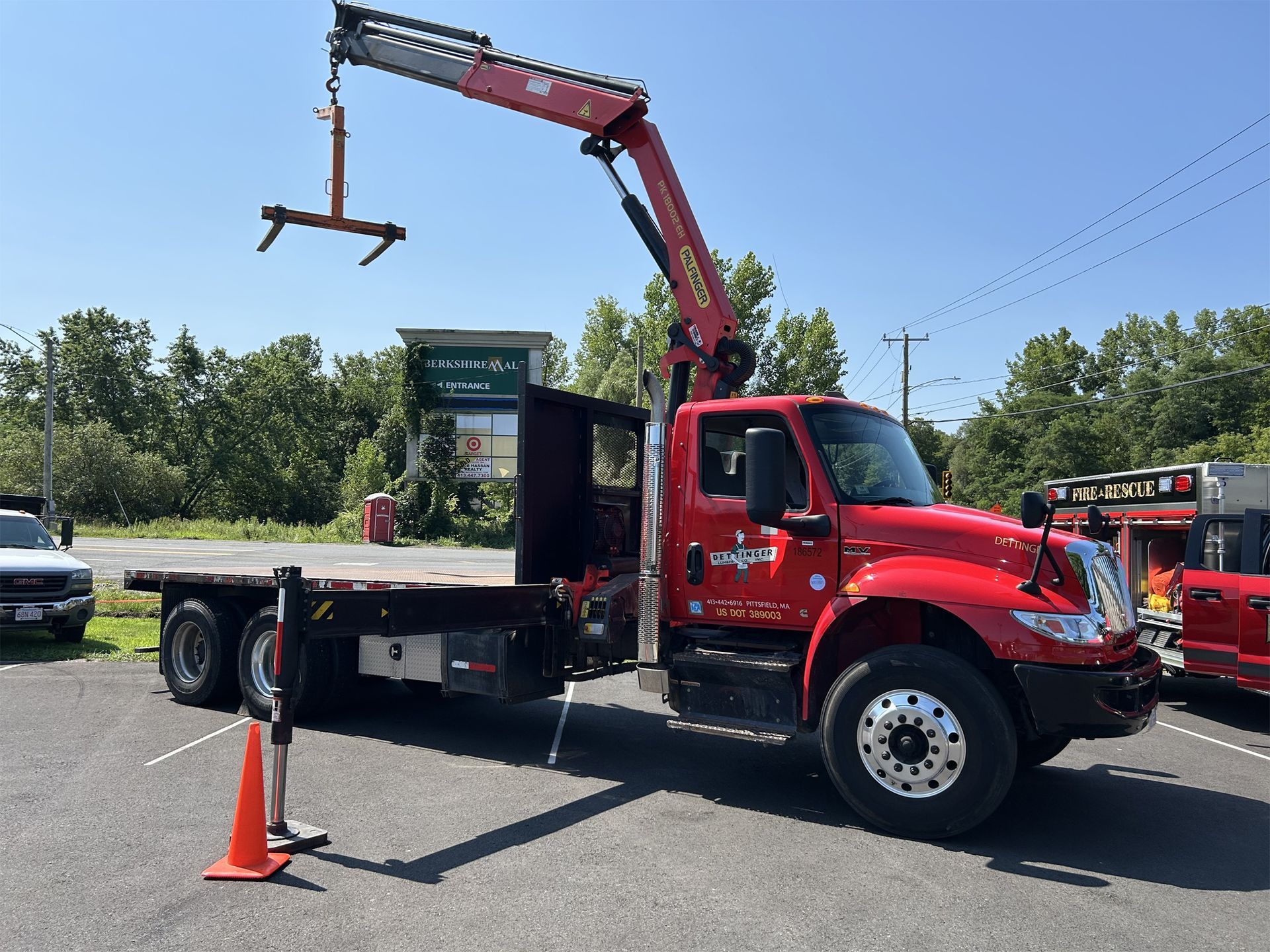 Red crane truck with an extended arm, parked outside, with a flatbed, and an orange cone.