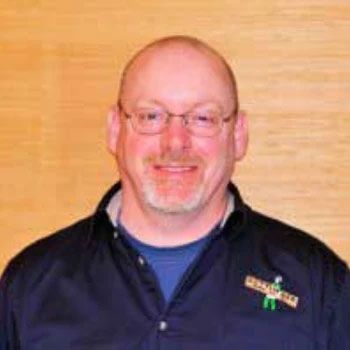 A bald man with glasses and a beard is wearing a blue shirt and a black jacket.