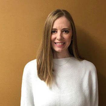 A woman in a white sweater is smiling in front of a brown wall.