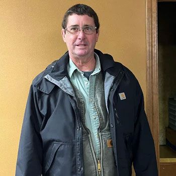 A man wearing a black jacket and glasses is standing in front of a wall.