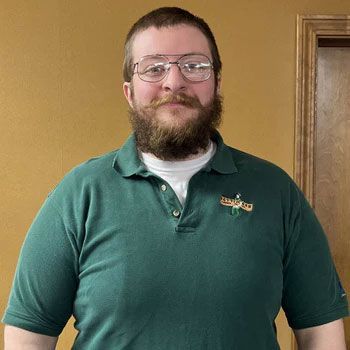 A man with a beard and glasses is wearing a green polo shirt.