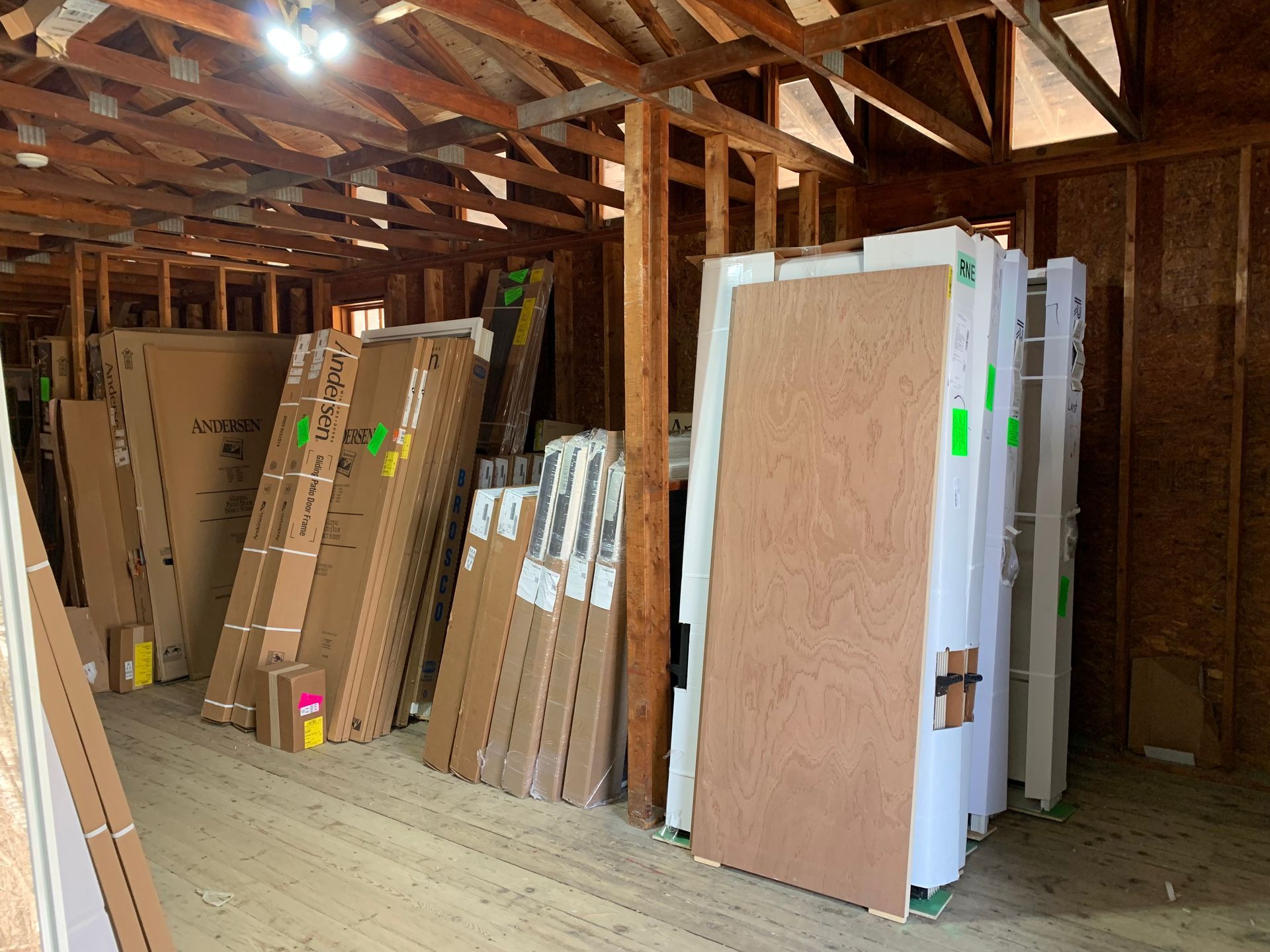 Inside a storage area filled with stacked new doors and building materials. The walls are wooden and the ceiling has exposed rafters.