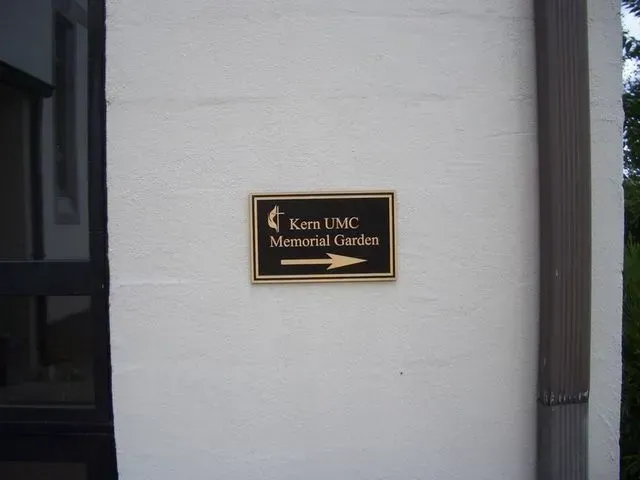 A bronze sign on a white brick wall points toward the Kern UMC Memorial Garden.