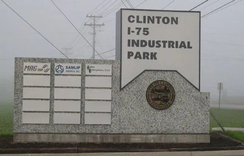 Sign for Clinton I-75 Industrial Park on a foggy day. Display panel with company logos, sign text, and a city seal.