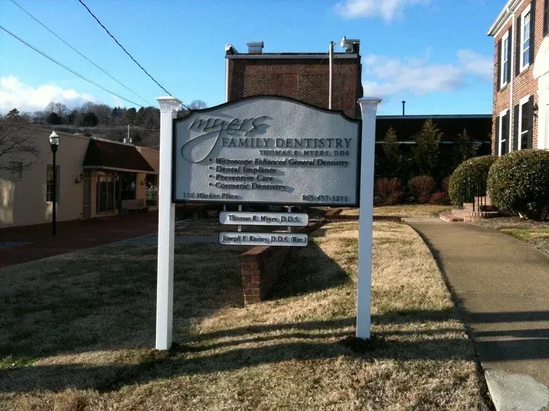 Sign for Miller's Family Dentistry, white posts, brick building in background, path to the right.