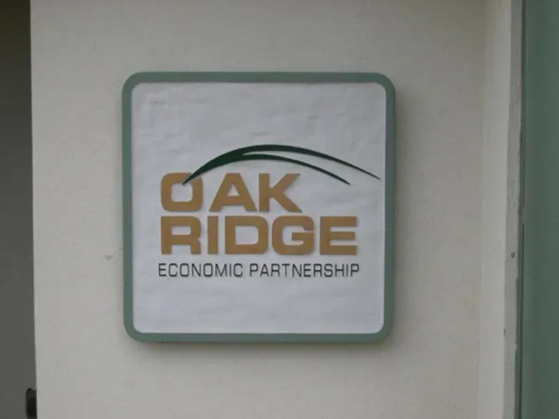 Sign for Oak Ridge Economic Partnership, square with green border and logo: green curved lines above tan 
