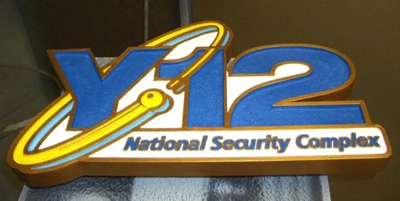 Y-12 National Security Complex logo with blue, white, and yellow colors on a brown background.