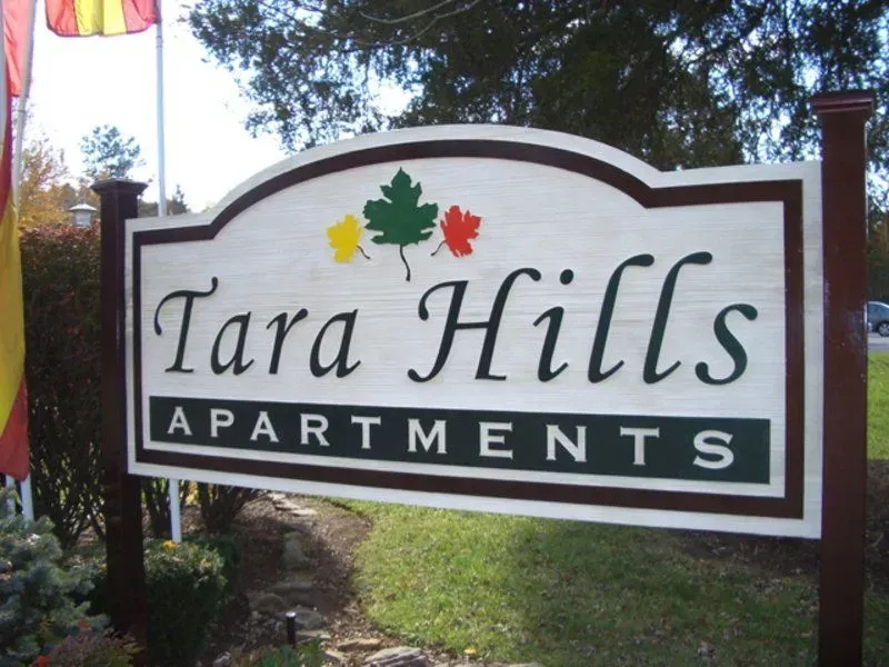 Tara Hills Apartments sign with green, yellow, and red maple leaf accents on a wooden background.