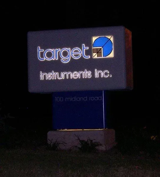 Illuminated sign for Target Instruments Inc. at night, featuring logo and address.