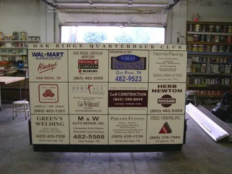 Sign with sponsor logos for the Oak Ridge Quarterback Club, displayed indoors.