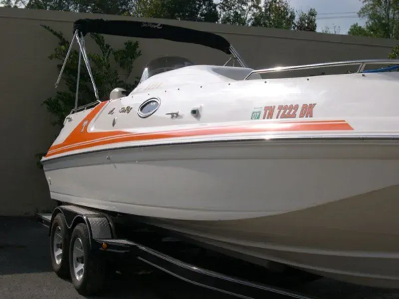 White and orange motorboat on a trailer, with a black bimini top, against a beige wall.