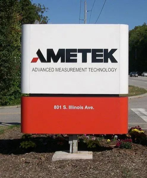 Sign for AMETEK Advanced Measurement Technology, white and orange, on a pole, with address 