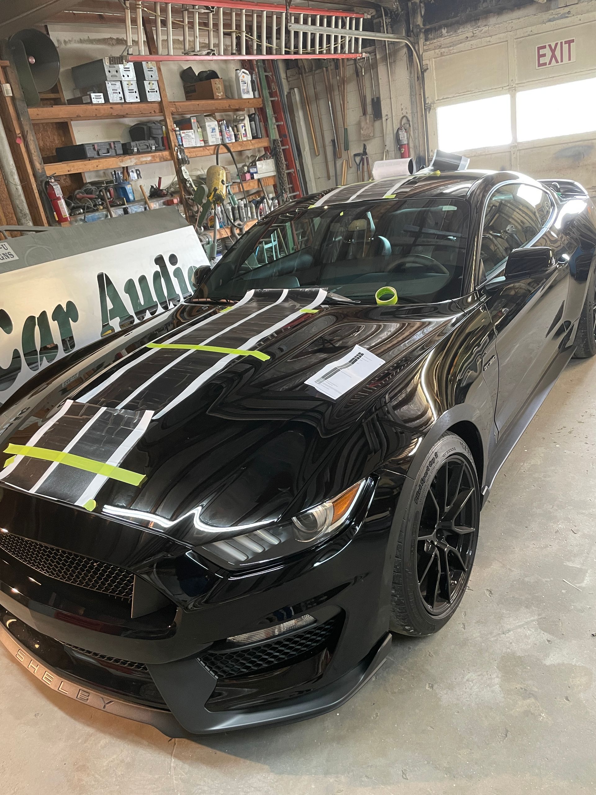 Black Ford Mustang with racing stripes in a car audio shop.