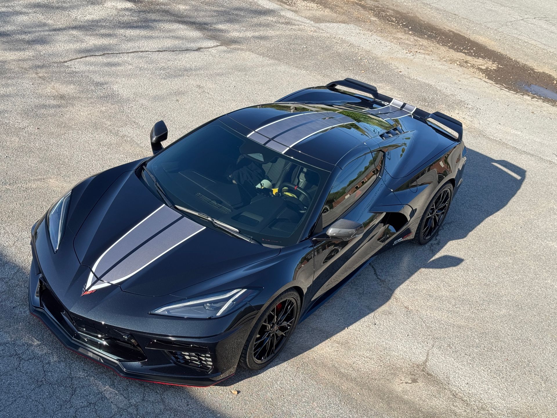Black Corvette sports car with gray racing stripes on asphalt.