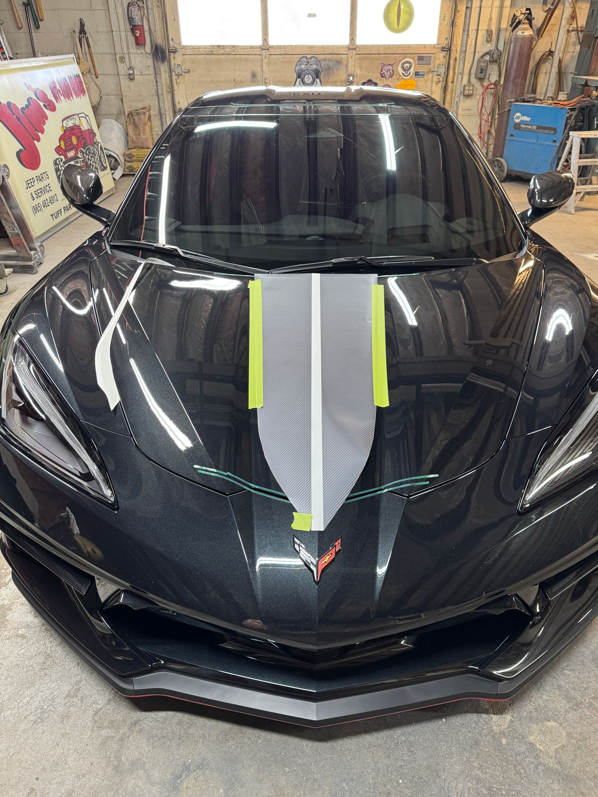 Black sports car with grey stripe detail, taped with green and white tape, in a workshop.