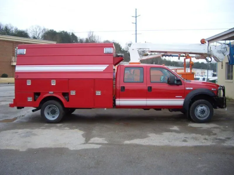 Red utility truck with a lift arm, parked outdoors.