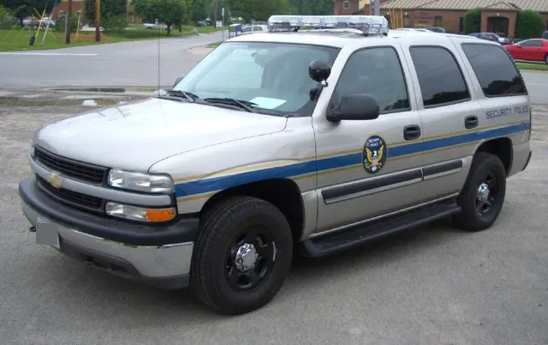 Silver Chevrolet Tahoe SUV with SECURITY POLICE text and blue stripe. Parked on asphalt.