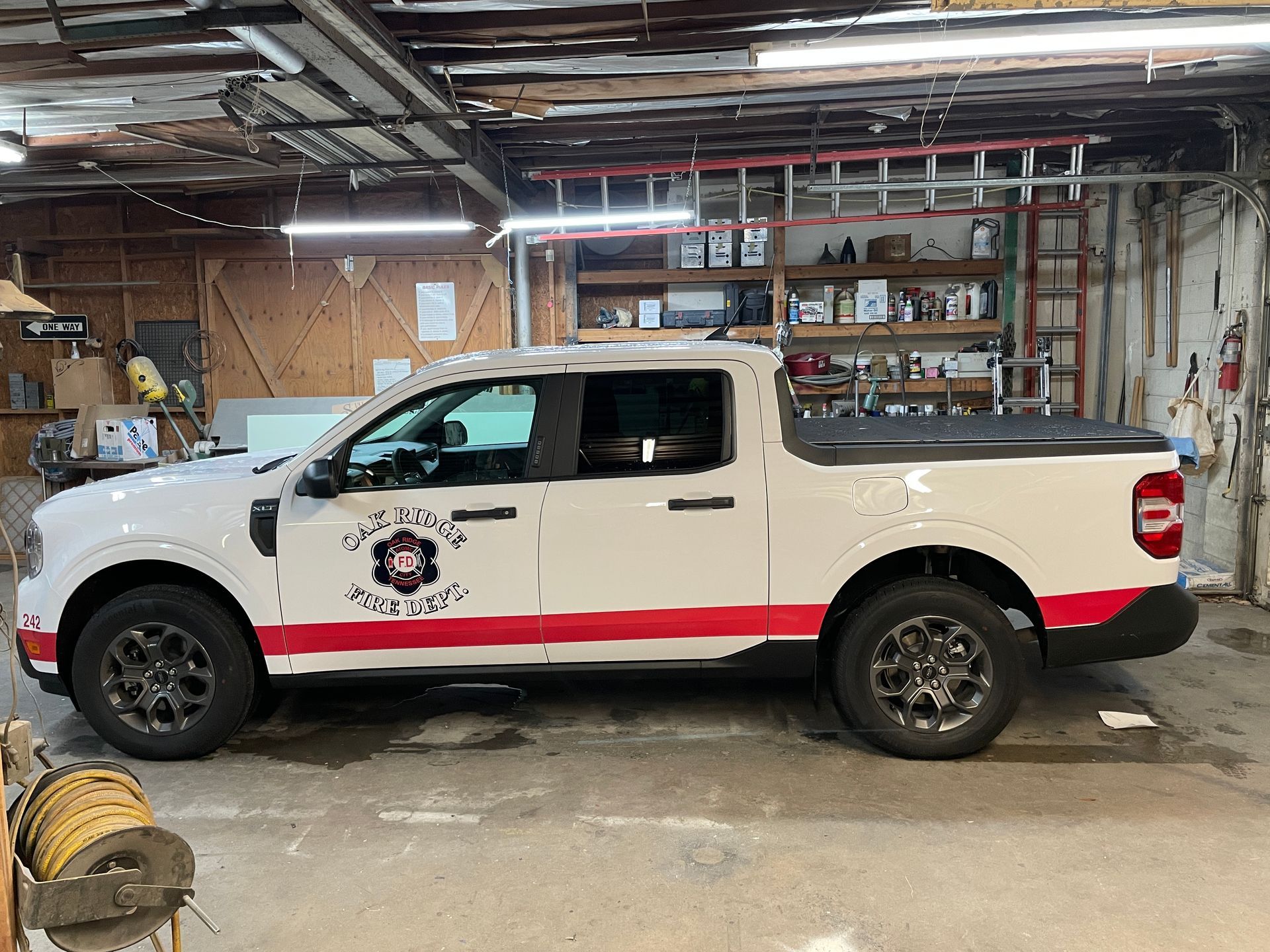 White and red pickup truck with fire department logo inside a garage.