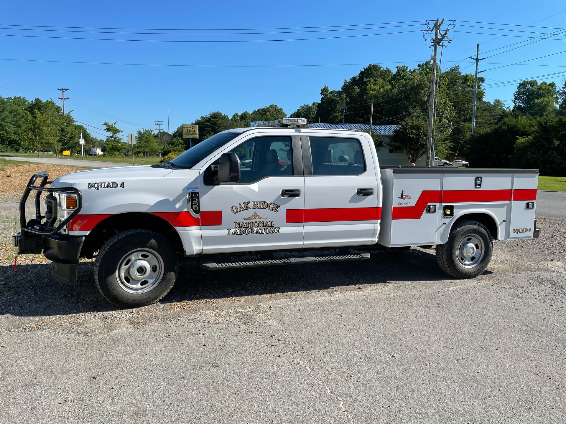 White and red utility truck with lettering, parked on gravel.