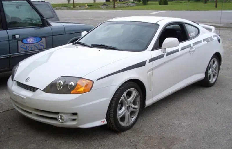 White Hyundai Tiburon with black side stripes parked outside.
