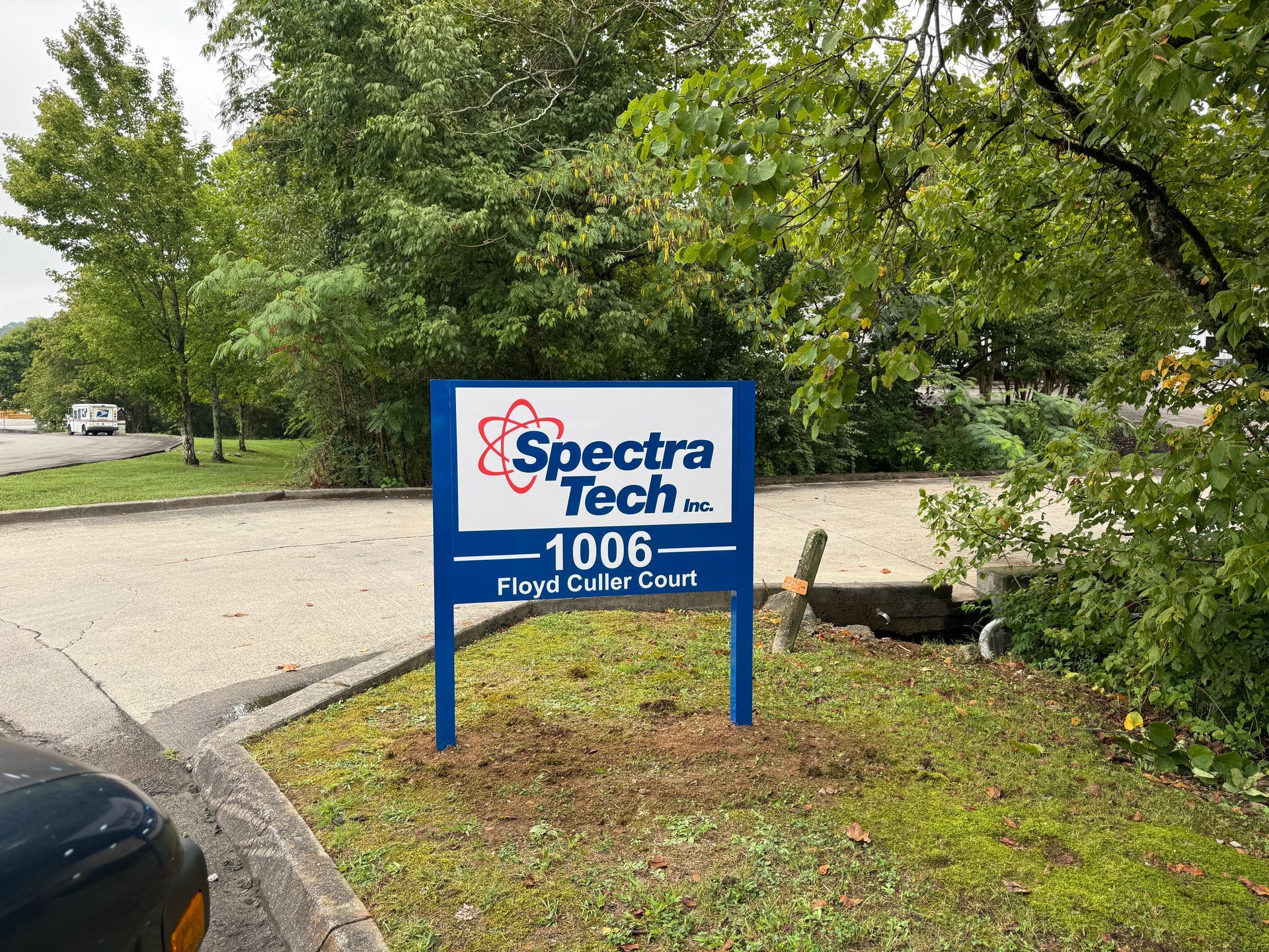 Sign for Spectra Tech Inc., blue and white, with address 1006 Royal Court, set in front of trees.