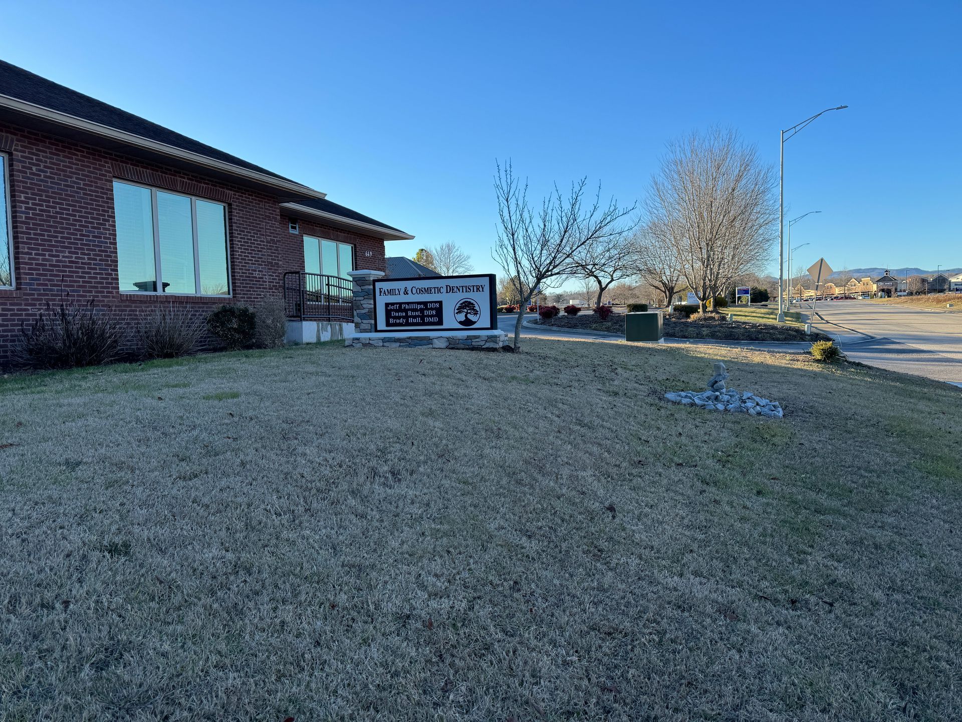 A brick building with tinted windows and a sign in front; a grassy lawn and a blue sky.