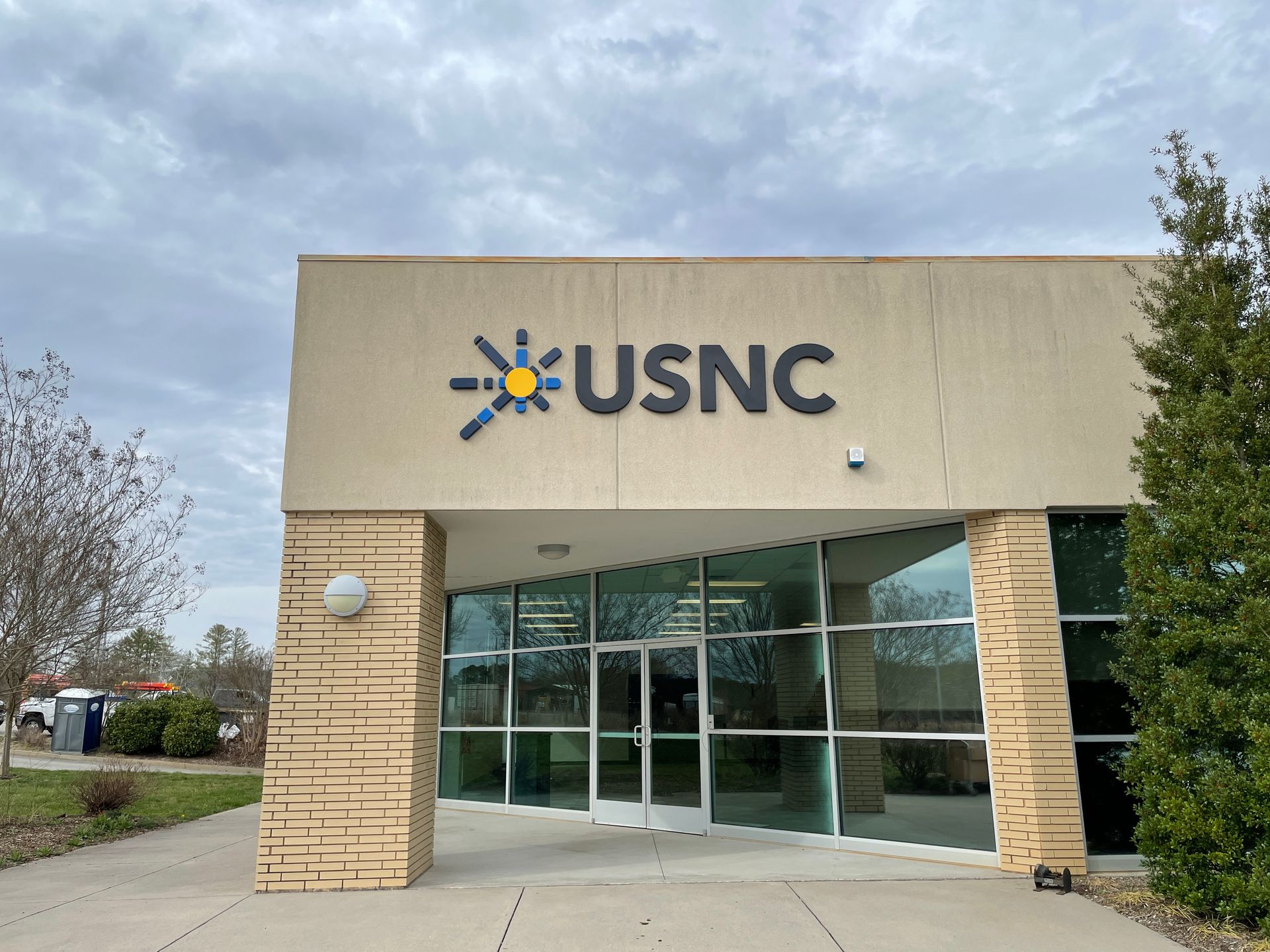 USNC building entrance with logo: blue and yellow sunburst, gray lettering, glass doors.