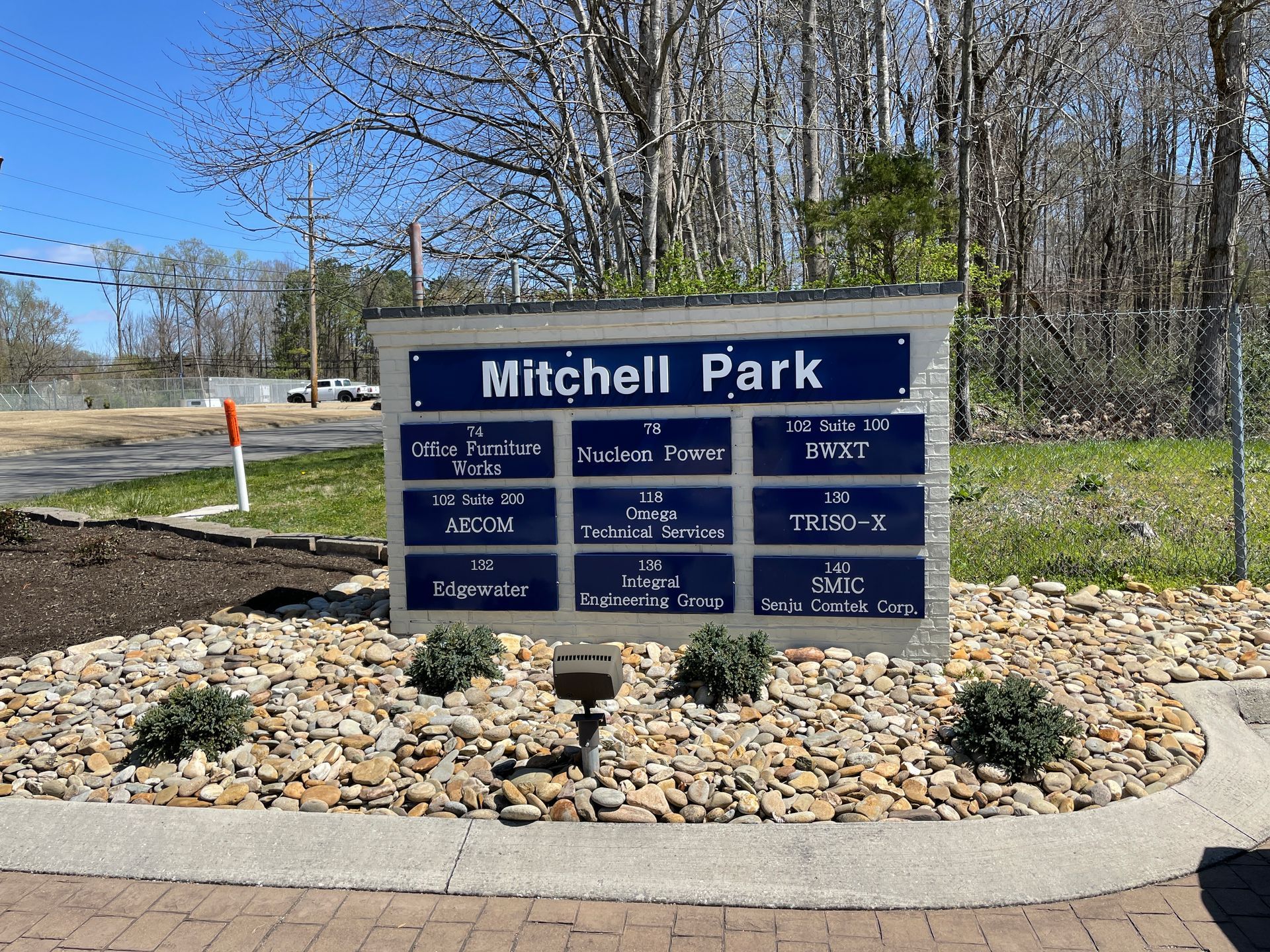 Mitchell Park sign with blue panels listing park amenities, set in a stone garden with trees in the background.