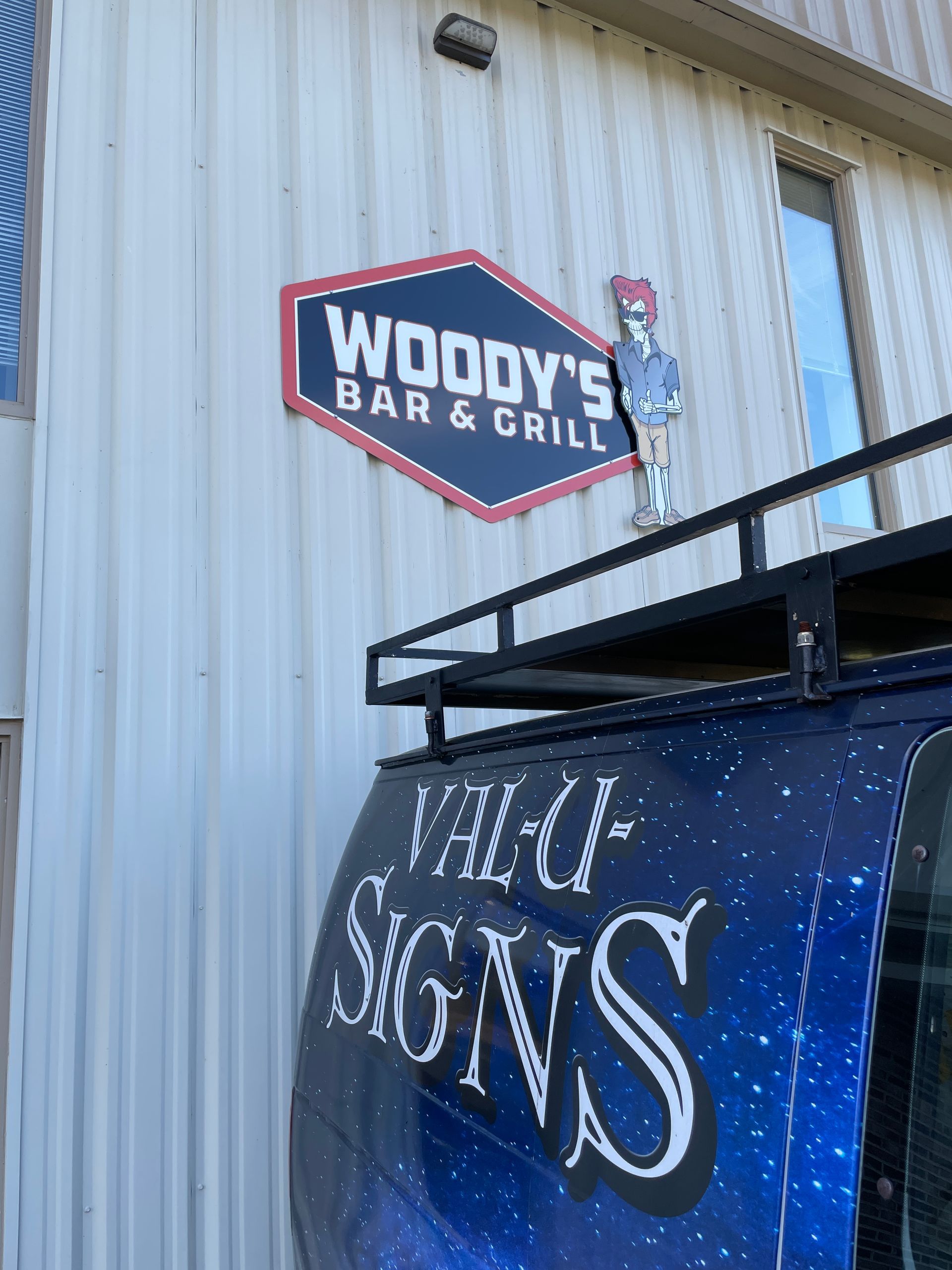 Sign for Woody's Bar & Grill above a van with 
