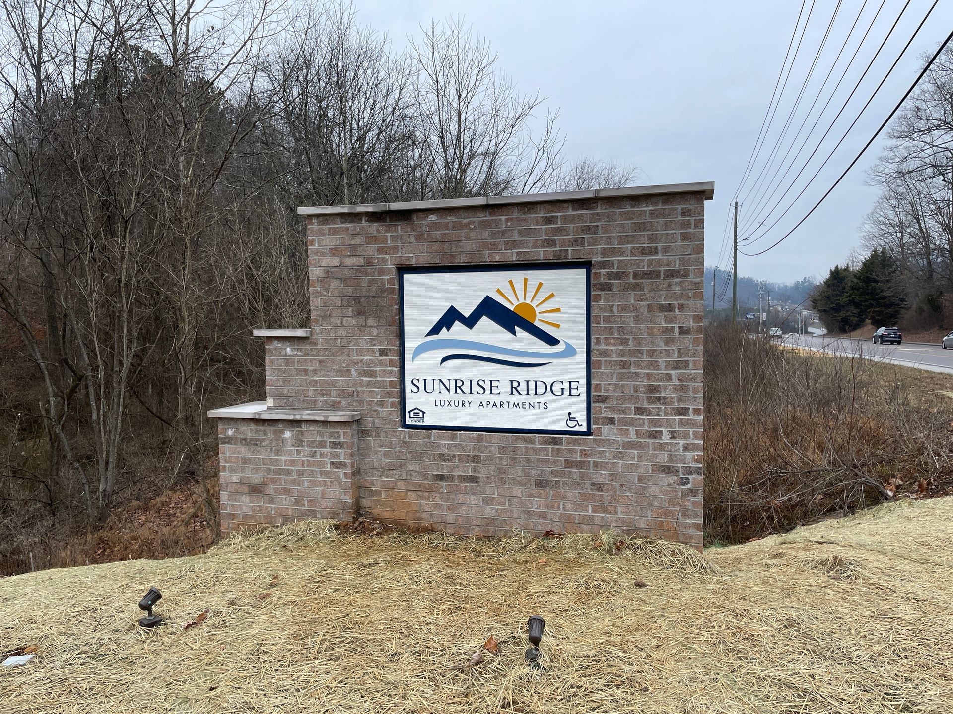 Brick entrance sign for Sunrise Ridge community, blue and yellow logo of mountains and sun.