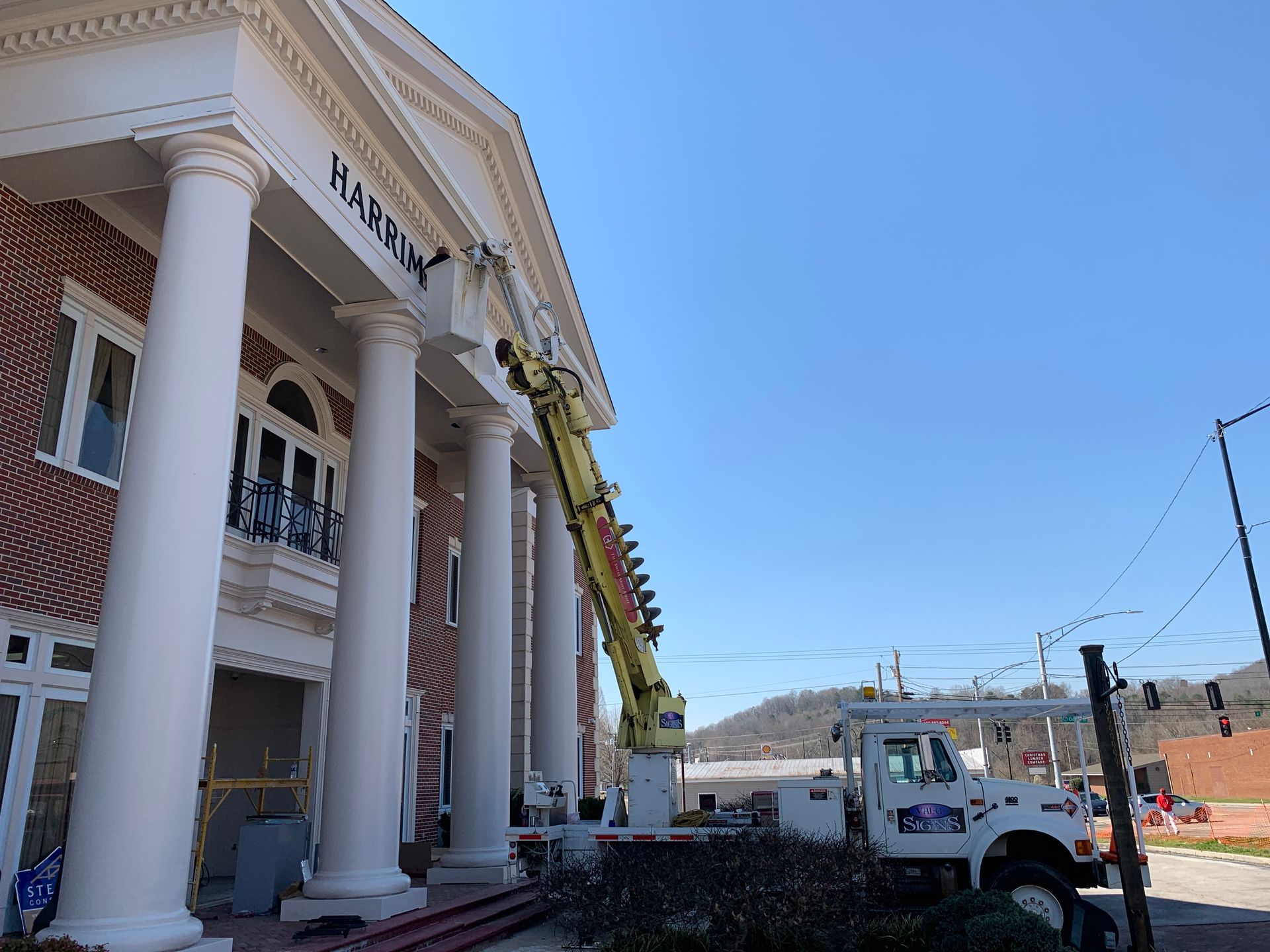 A cherry picker truck works on the front of a brick building with white columns; a sign says 