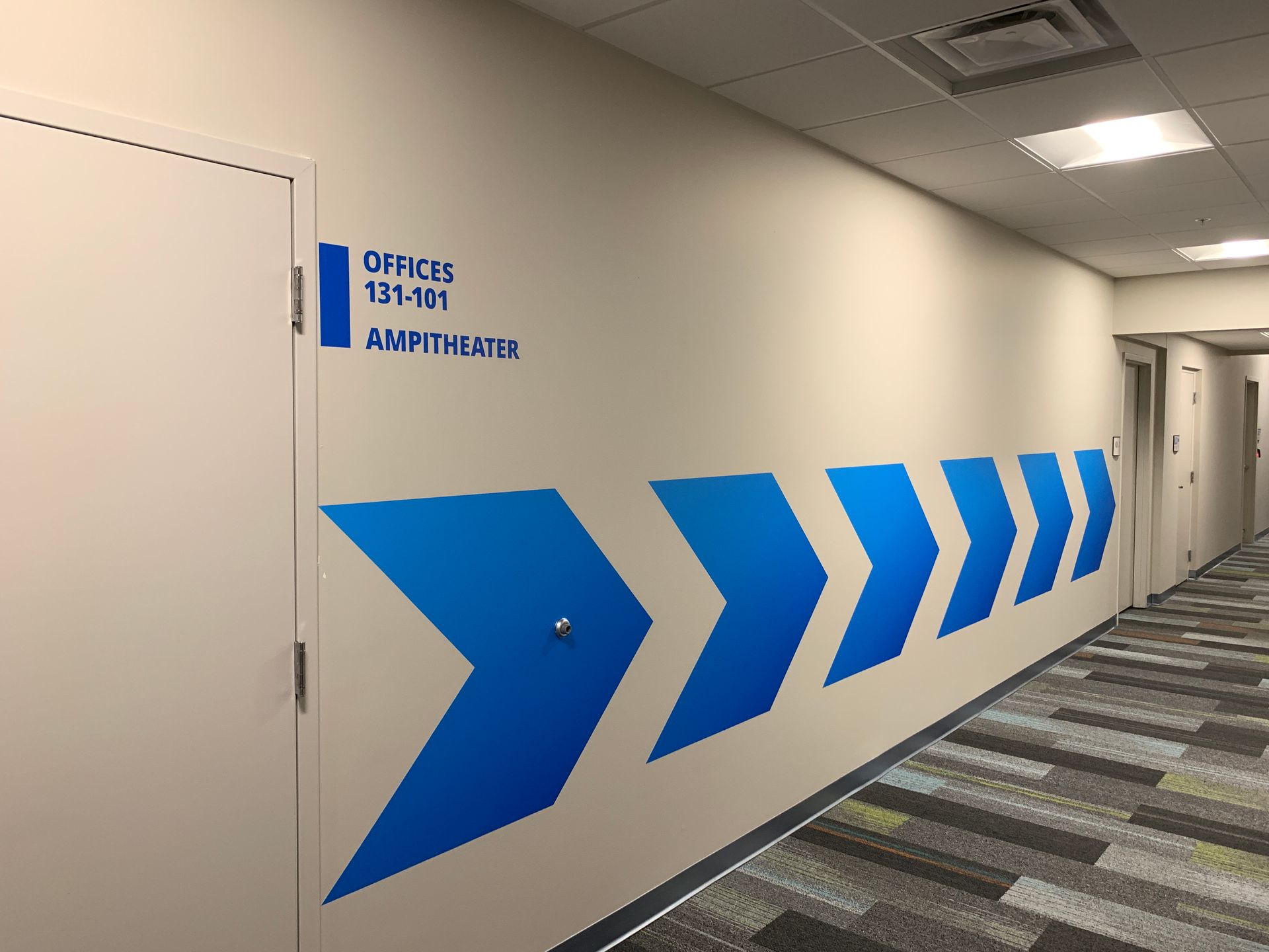 Hallway with blue directional arrows on a white wall. Sign reads 