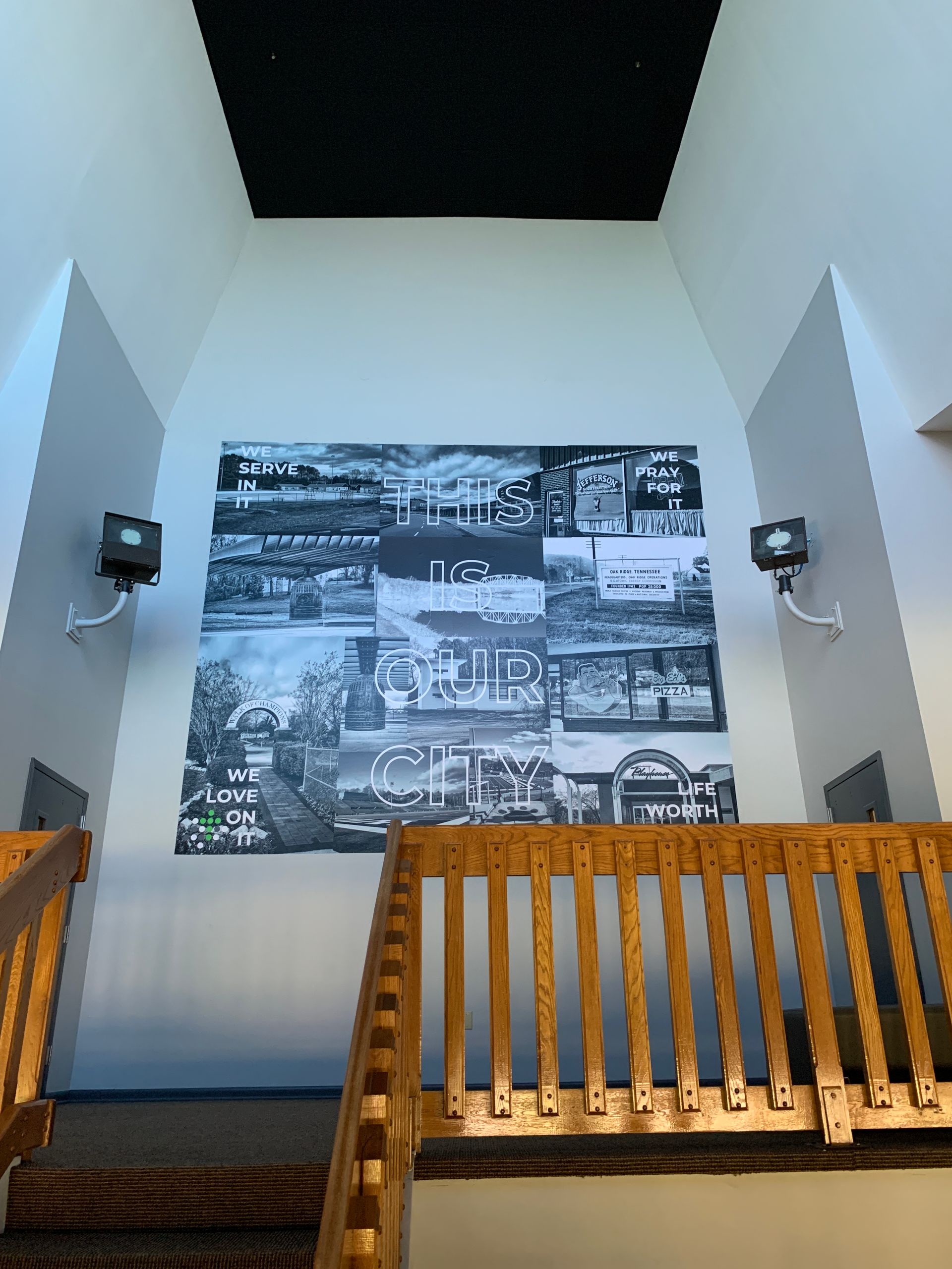 Staircase leading to a large wall collage of black and white photos, flanked by speakers, beneath a black ceiling panel.