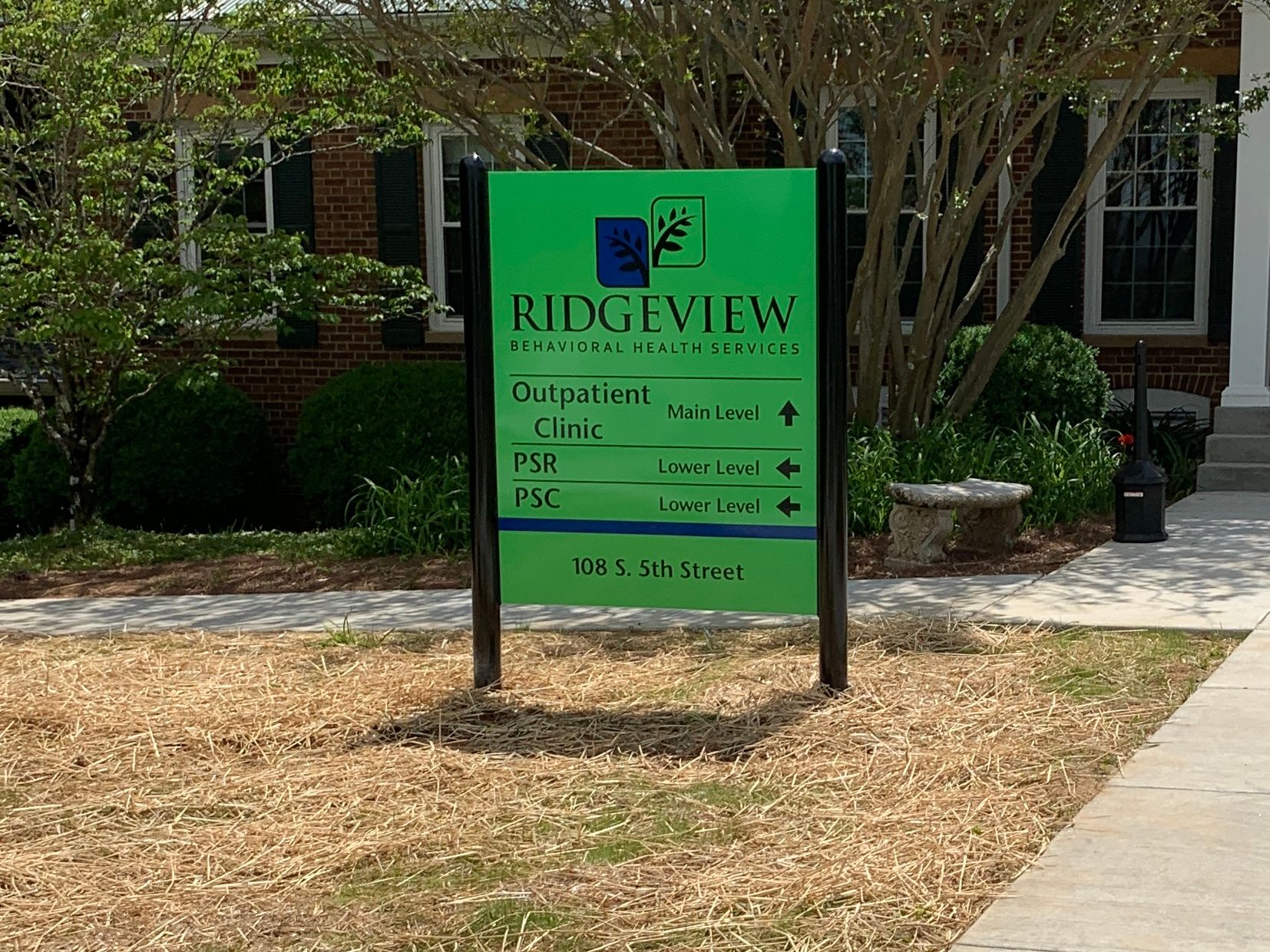 Sign for Ridgeview with directions and logo; green background, black text, brown landscaping.