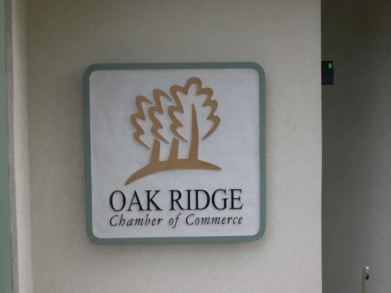 Oak Ridge Chamber of Commerce sign with a logo of two stylized trees. White background, green border, on a building wall.