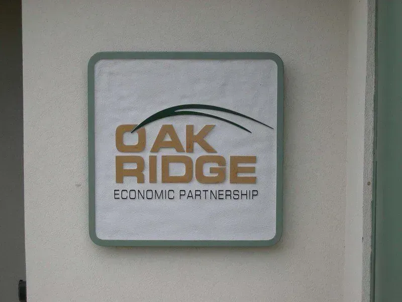 Sign for Oak Ridge Economic Partnership, square with green and gold lettering on white, mounted on a wall.