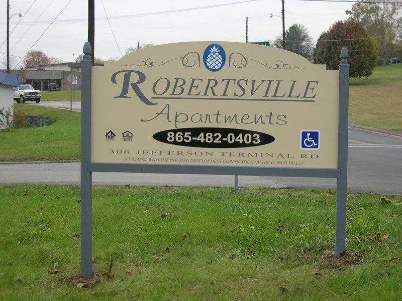 Sign for Robertsville Apartments, tan background, blue logo, phone number, address, accessible symbol.