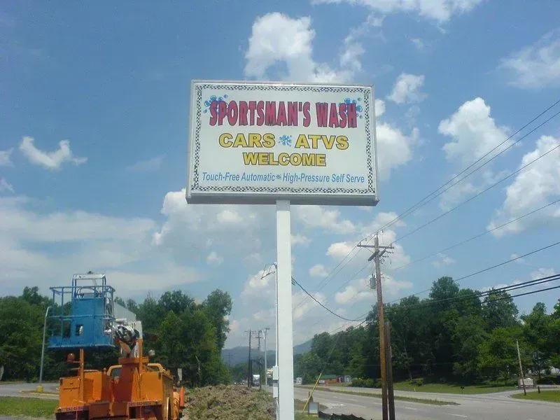 Sign for Sportsman's Wash, offering car and ATV cleaning. Blue sky, white sign on a pole, with trees in the background.