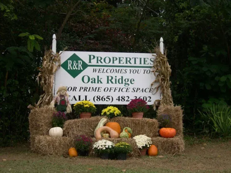 Sign for R&R Properties in Oak Ridge, TN. Decorated with hay bales, pumpkins, and flowers.