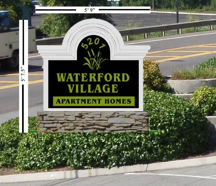 Sign for Waterford Village Apartment Homes, with brick base and landscaping, set on a road with a guardrail.