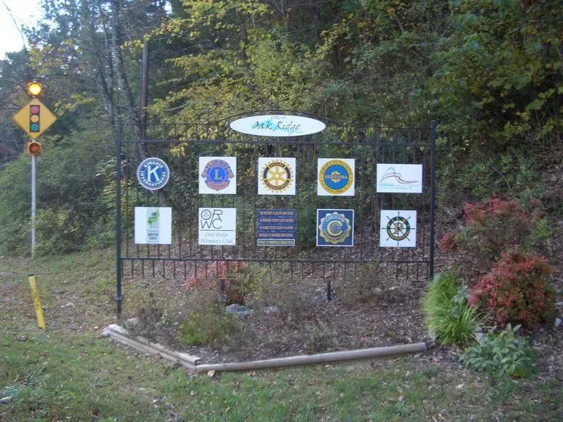 Sign with logos of various organizations, near roadside plants and a traffic light.