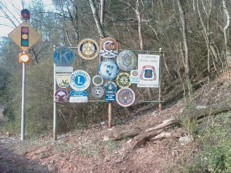 Sign with club logos next to a traffic light in a wooded area.