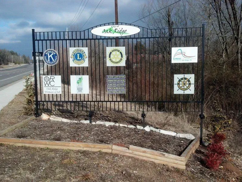 Black metal community sign with several organizational logos and a welcome sign.