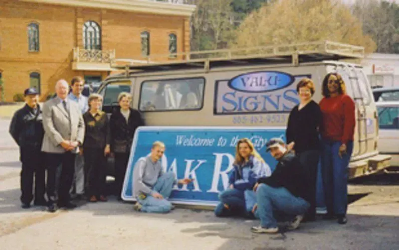 Group of people pose with a blue and white sign that says 