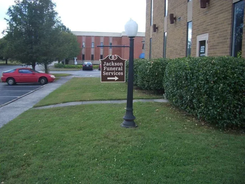 Sign for Jackson Funeral Services with a red car and building in background.