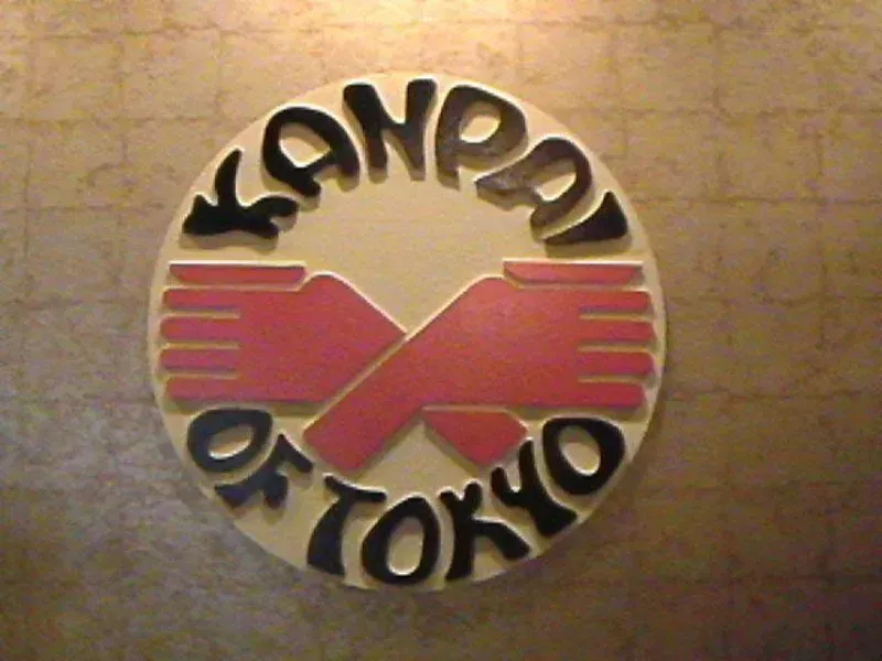 Kanpai of Tokyo restaurant logo: Black text in a circle, red hands clasped.