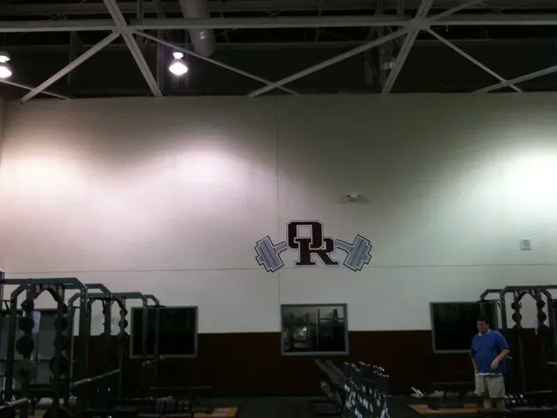 Weight room with weightlifting equipment. A logo 