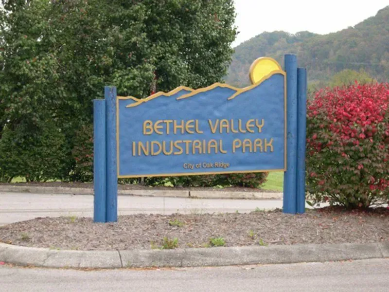 Sign for Bethel Valley Industrial Park, blue with gold lettering, roadside, trees, and mountain backdrop.